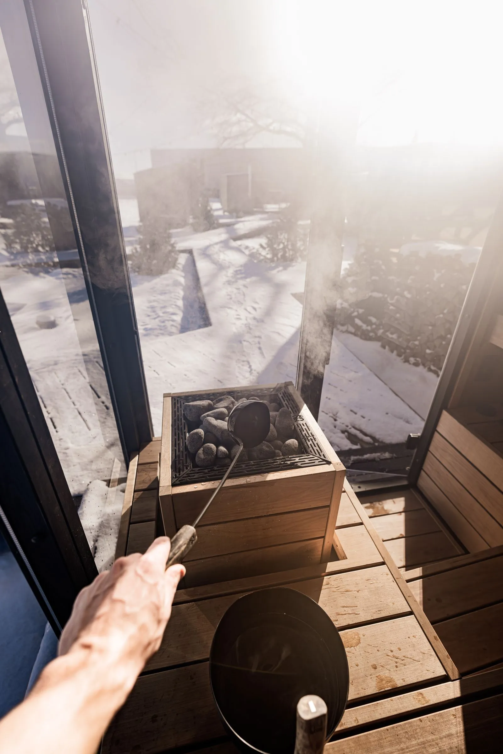 Sauna window looking out onto deep snow, stones on the heater in the foreground