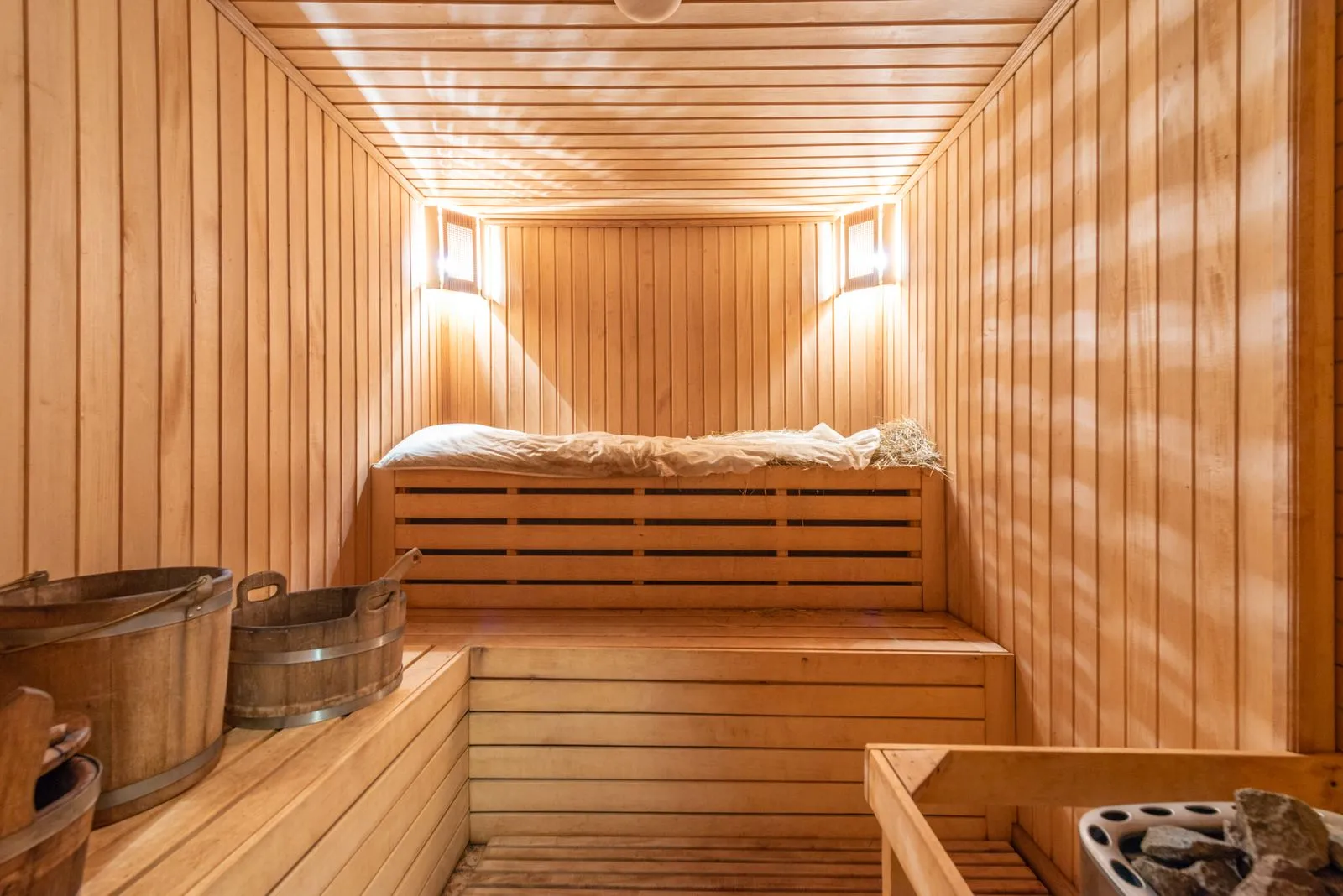 Warm cedar-lined Finnish sauna interior with wooden benches, buckets and soft lighting