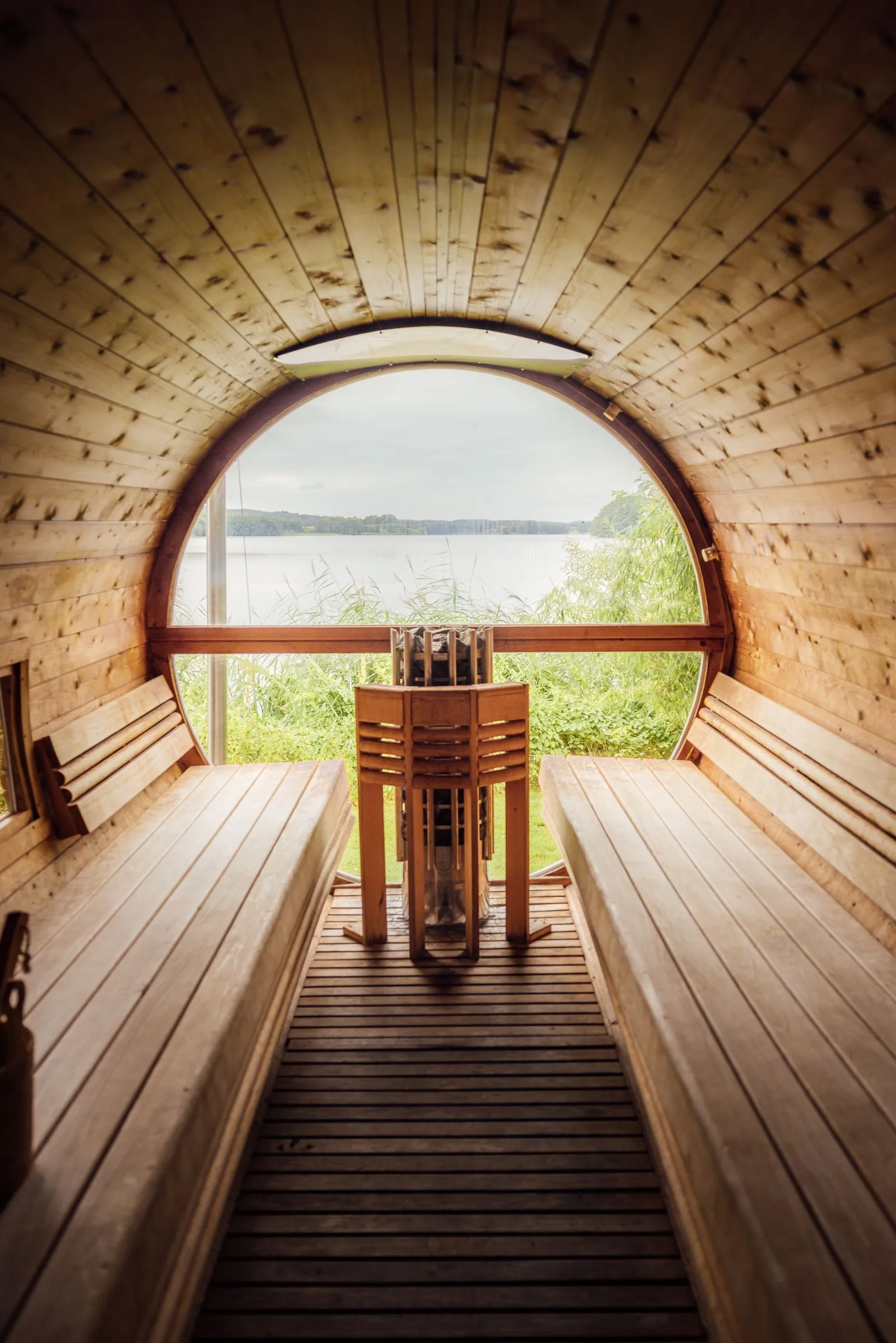 Barrel-style sauna beside a lake with loungers on a deck