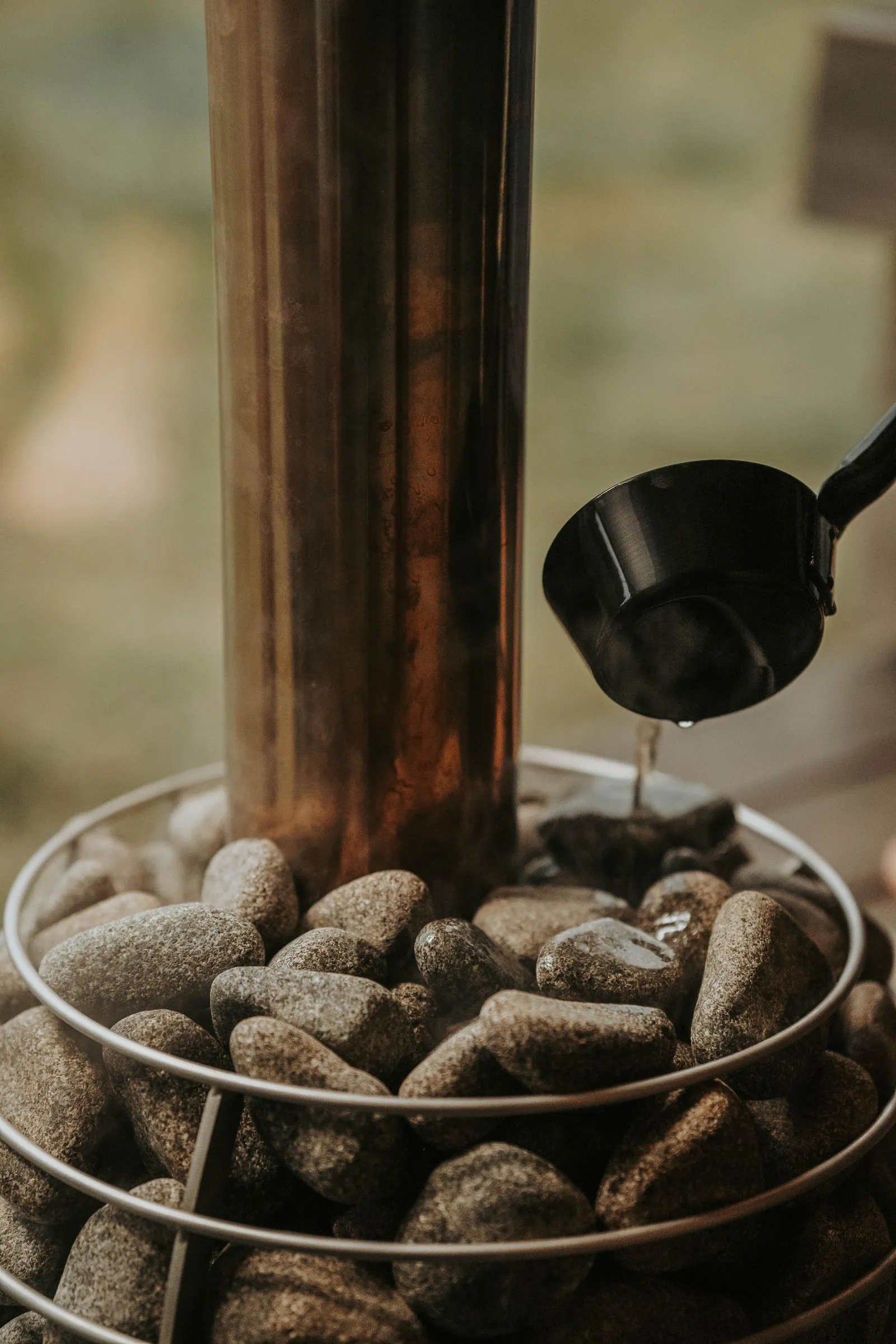 Water being ladled over dark sauna stones around a heater flue