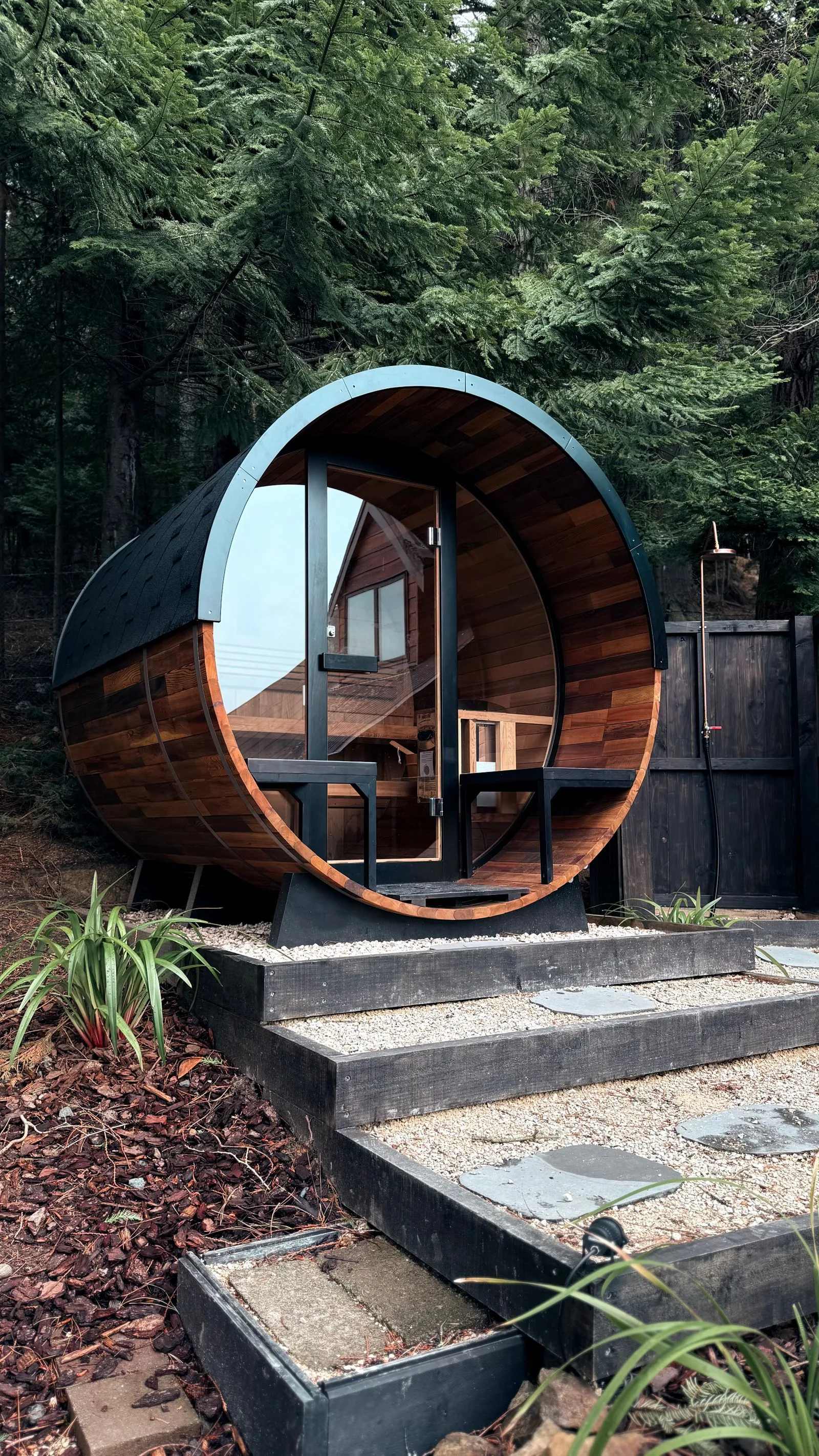 Modern round outdoor sauna with a large window set in a wooded backyard