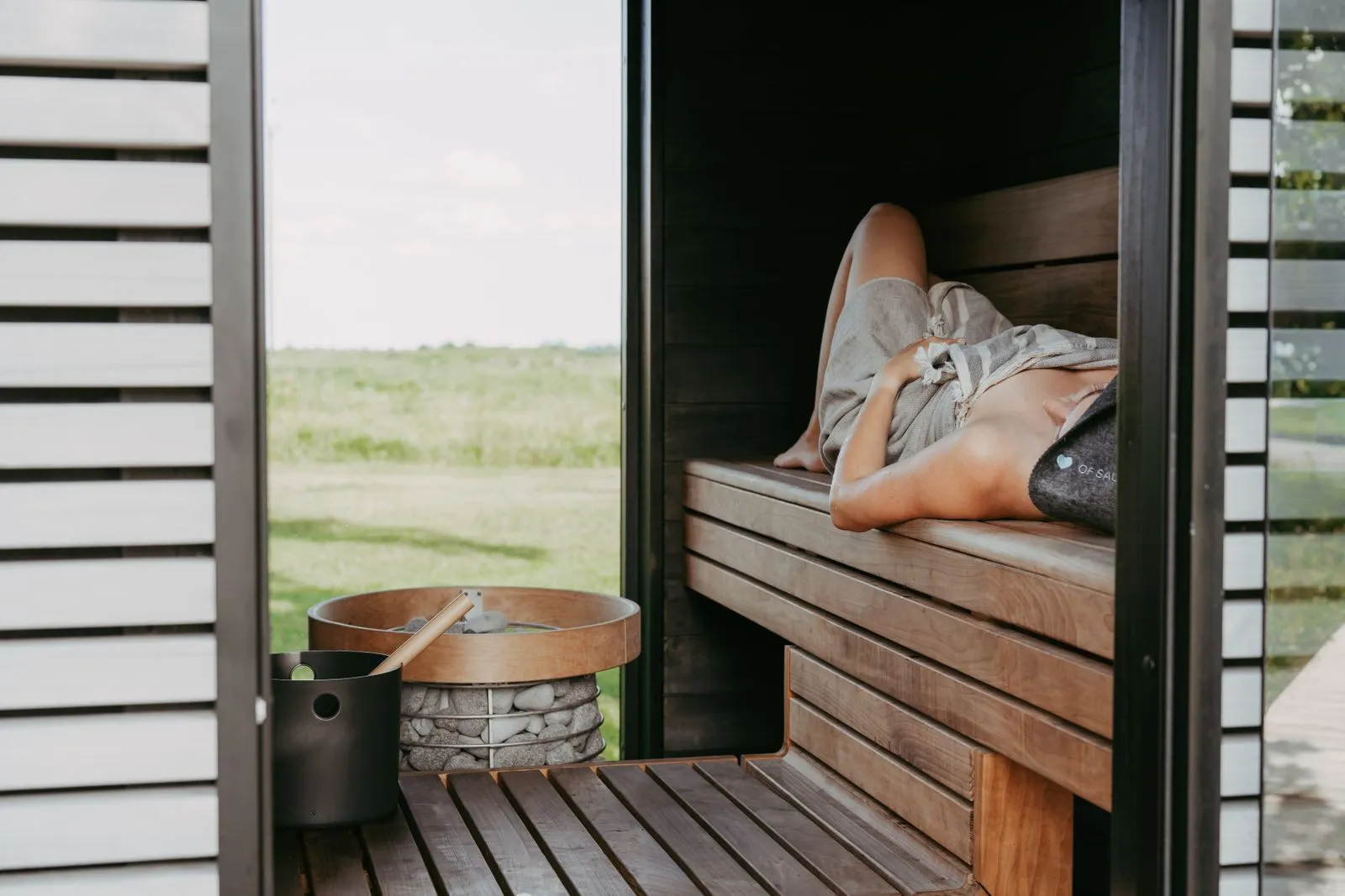 Person relaxing on the bench of a modern light-wood sauna cabin