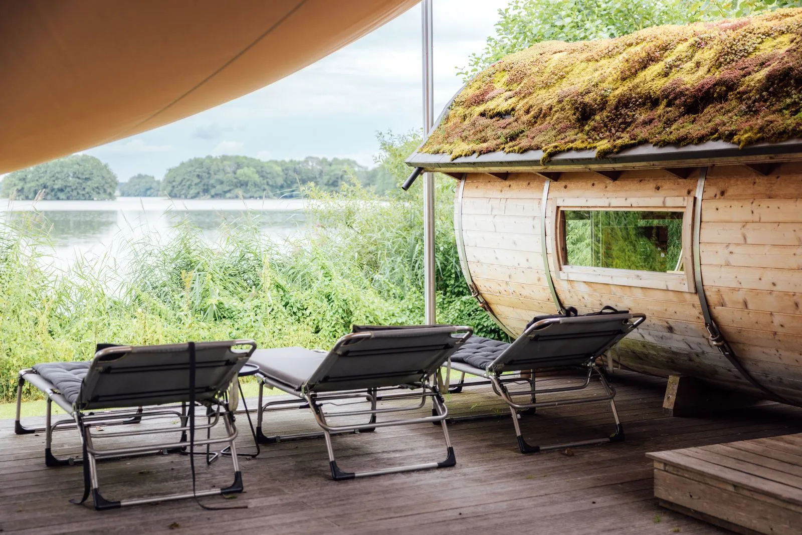 Lakeside barrel sauna with loungers on a wooden deck by the water